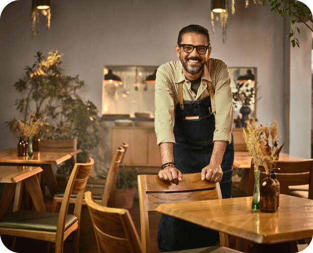 Na imagem consta um homem sorridente de avental em restaurante aconchegante.
