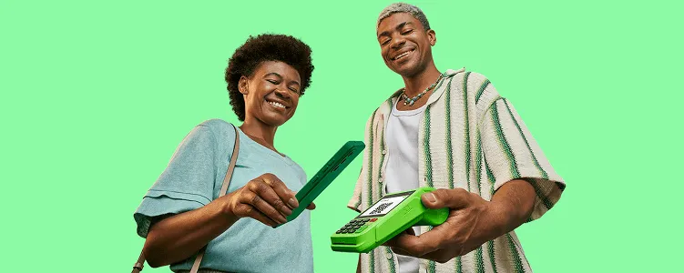 Empreendedor sorrindo, segurando a maquininha do Ton em sua mão esquerda, uma cliente está em sua frente também sorrindo e aproximando seu celular sobre a tela da maquininha para ler o QR Code que aparece na tela e realizar um pagamento via Pix.